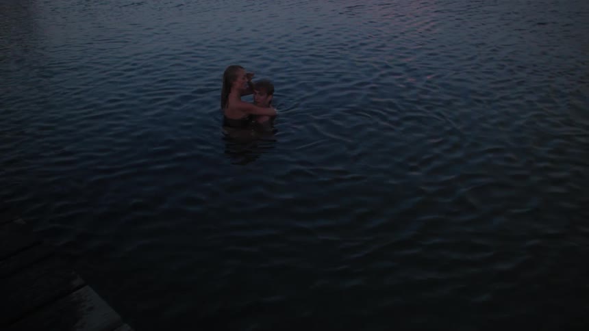 A man and woman hug while swimming