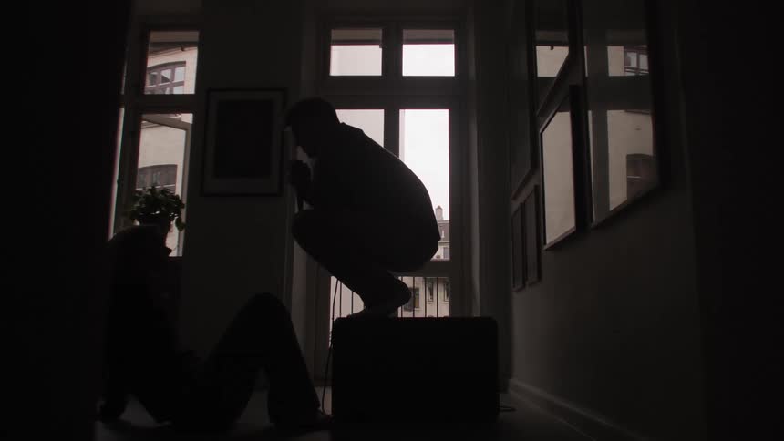 Silhouette of a man on top of a box singing to a woman watching sitting on the floor