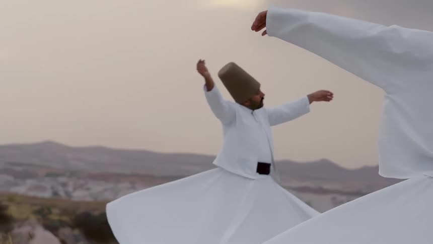 Two men in traditional sufi dress dance outdoors spinning with their hands lifted and eyes closed