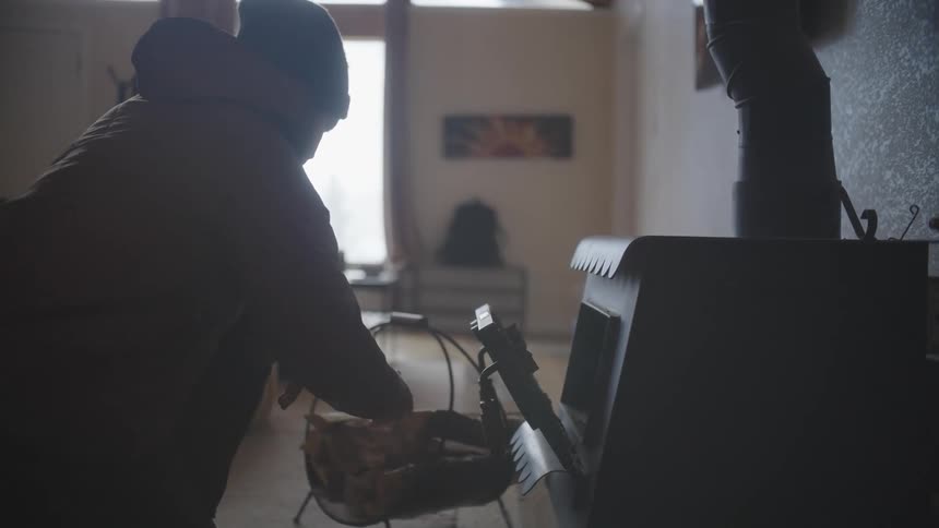 A person wearing winter clothes places chopped wood into a furnace