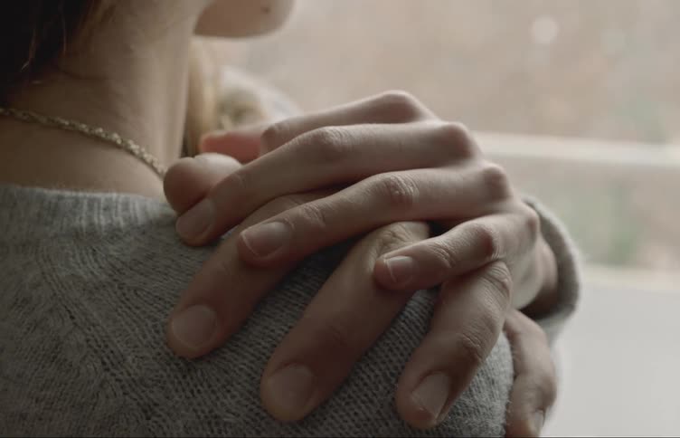 A closeup of two peoples hands touching gently over someones shoulder