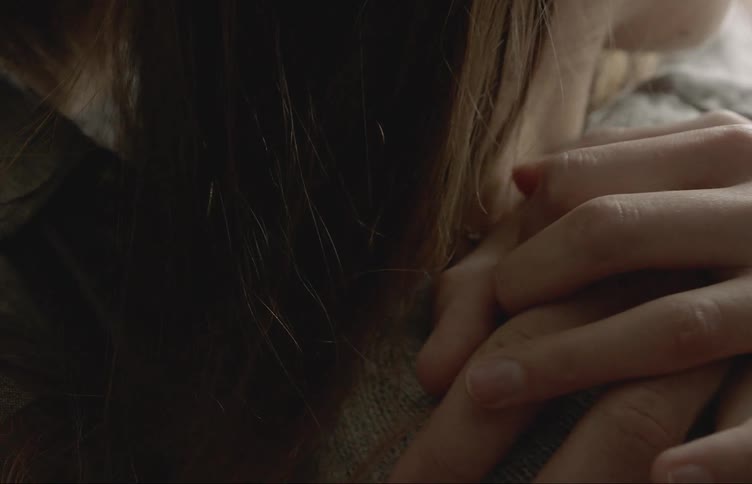 A woman looks out a window when a mans arm hugs her from behind and she holds his hand tightly on her shoulder