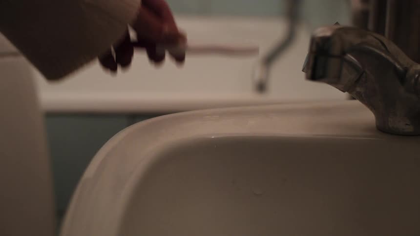 A womans hand picks up a pregnancy test from a bathroom sink