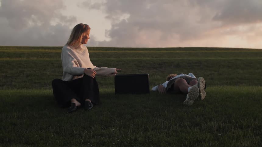 A young man sits back and relaxes on a grassy field with a female companion