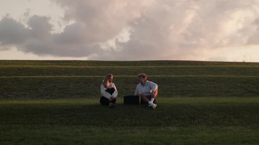 A man and a woman are sitting in a grass field and talking