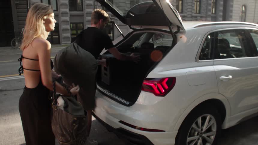 A man and a woman put luggage into the trunk of a car