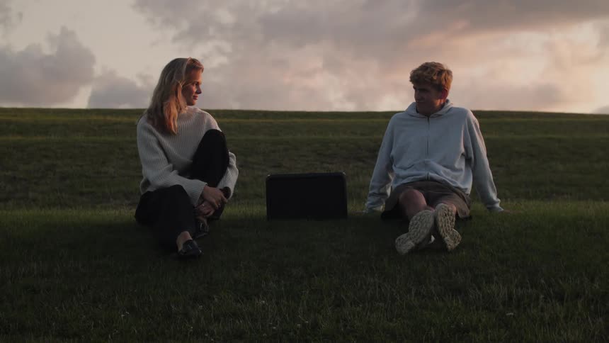 A man and a woman sit on the grass around an object and are shaking their heads