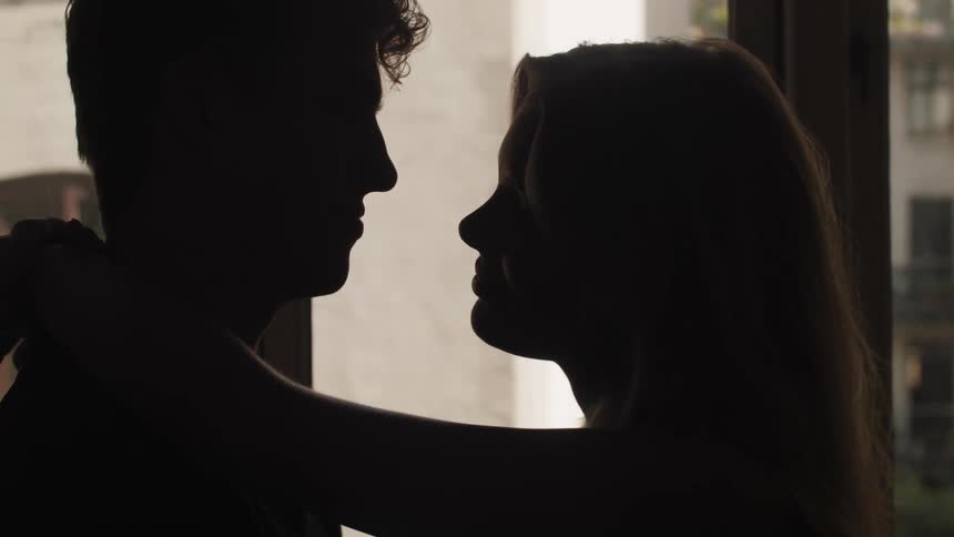 A man and woman embrace each other in front of a large window