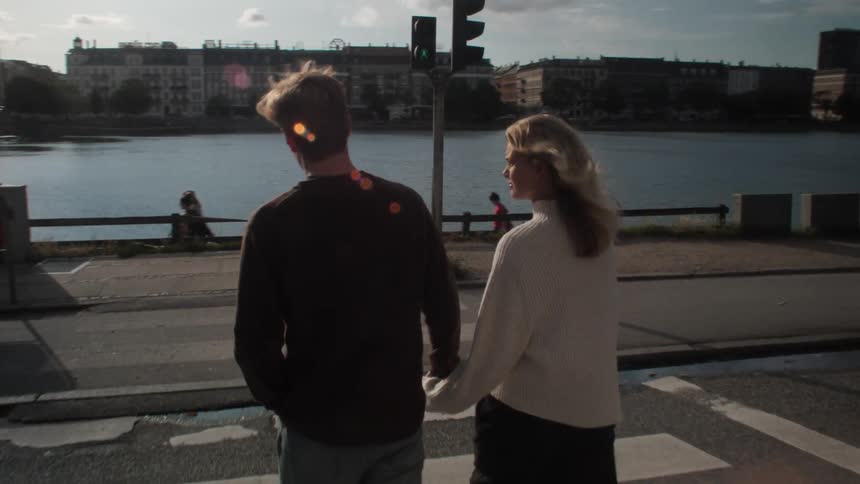 A couple crosses a road on a crosswalk while holding hands to get to a city river