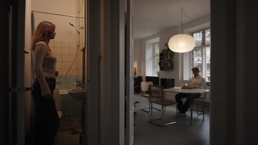 A woman is looking at herself in the bathroom mirror and soon finds herself with a man who was sitting on a laptop in the other room