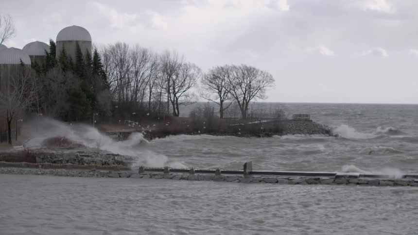 Waves crash across a shoreline and jetty on a cold day