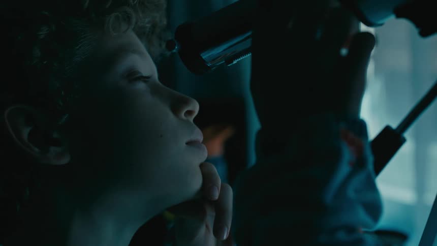 A boy looks through his telescope out the window