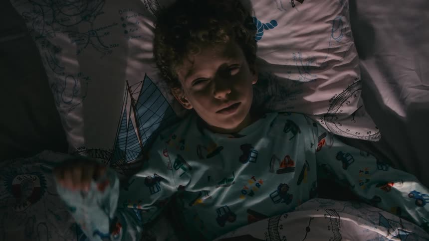 A boy wakes up in his bed and stretches as he turns around and sits up