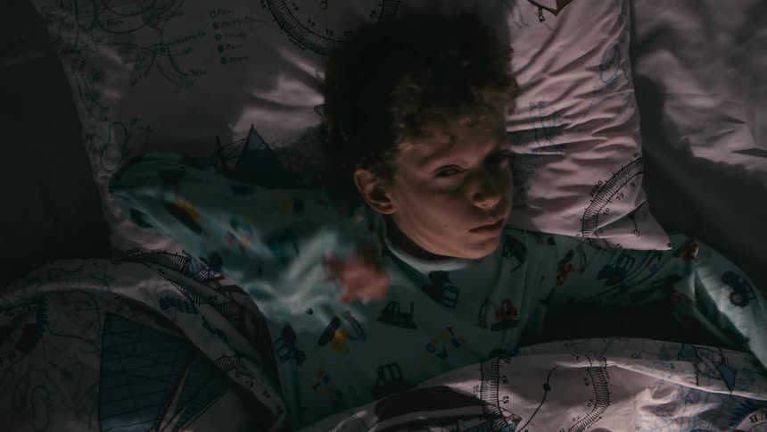 A boy wakes up in his bed and stretches as he turns around and sits up
