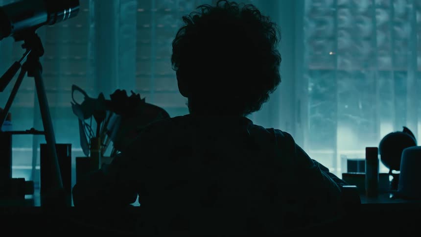 Silhouette of a young boy sitting at a desk writing in a dark room