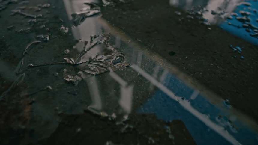 A dirty puddle of water in the street reflecting a building