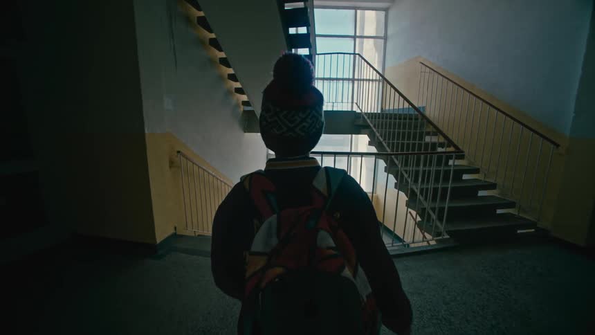 Back view of a boy walking in a corridor and going down the stairs of a building