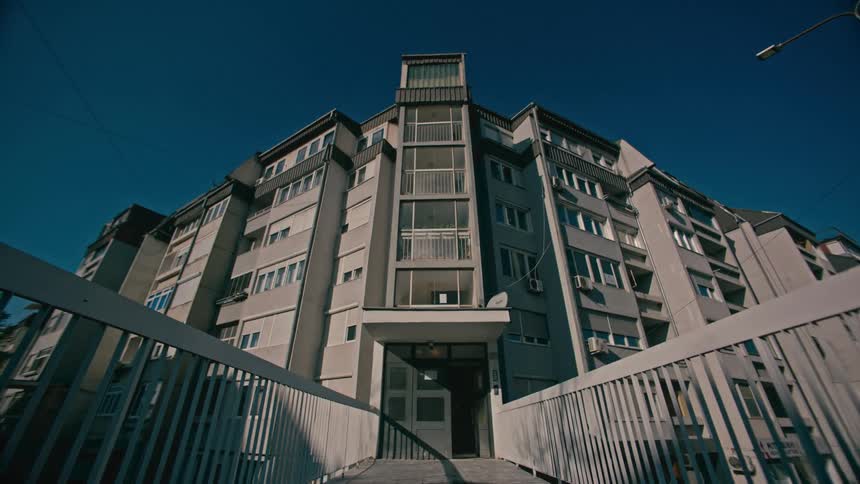 A large building with balconies and a tower under a blue sky surrounded by fences