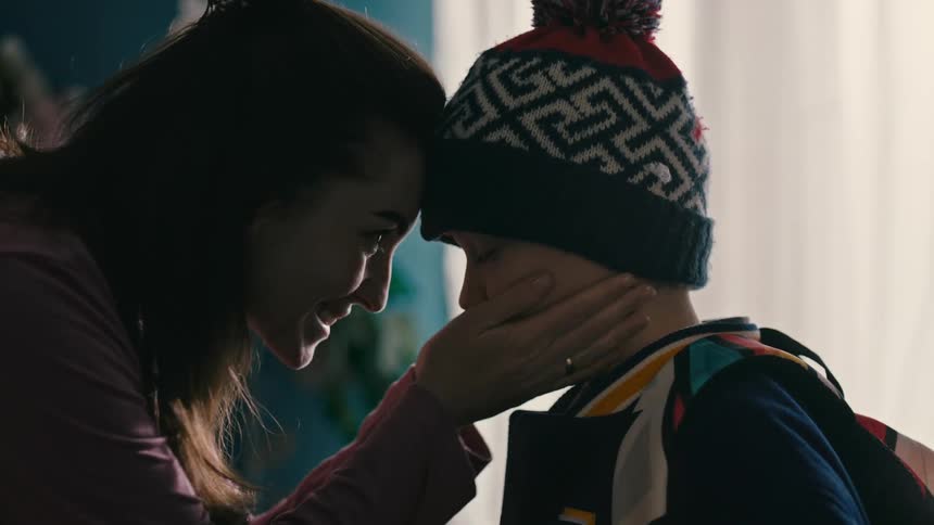 A mother is helping her son put on a colorful knit cap indoors