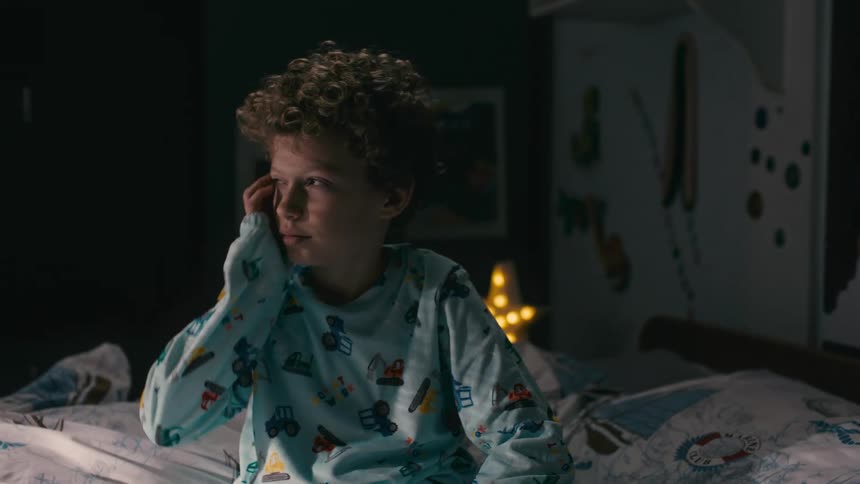 A boy in pajamas is sitting on the bed and is tired and gets up from his bed