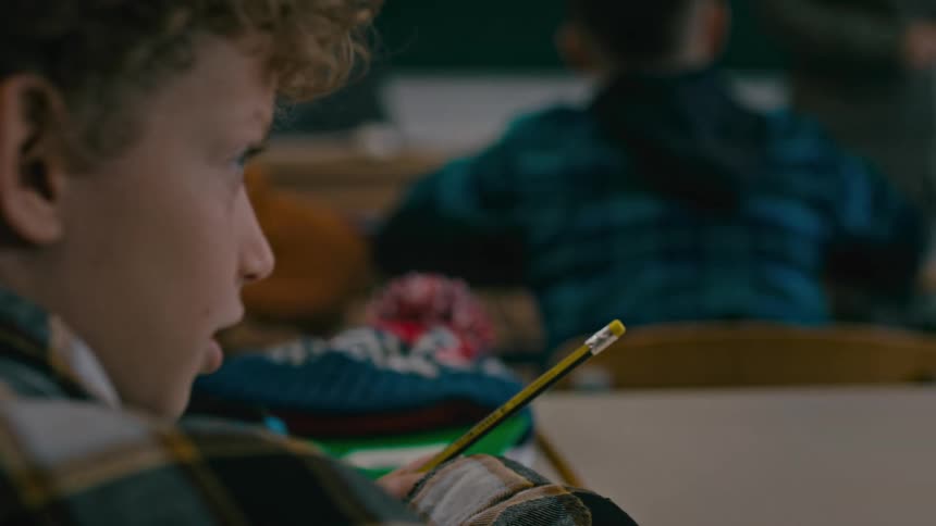 A boy talks to a girl in school as the teacher approaches