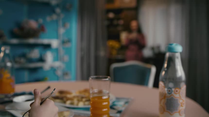 Mother standing in the kitchen watches his son eat breakfast