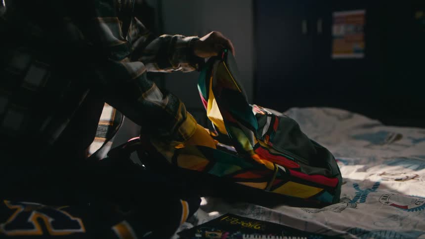 A young boy in his bedroom packs his backpack while getting ready for school