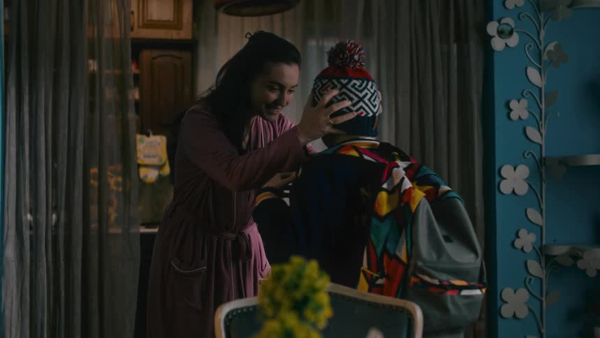 A mother is helping her son put on a colorful knit cap at home