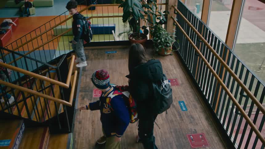 View of a hallway with stairs with a boy bumping into another and knocking over his books
