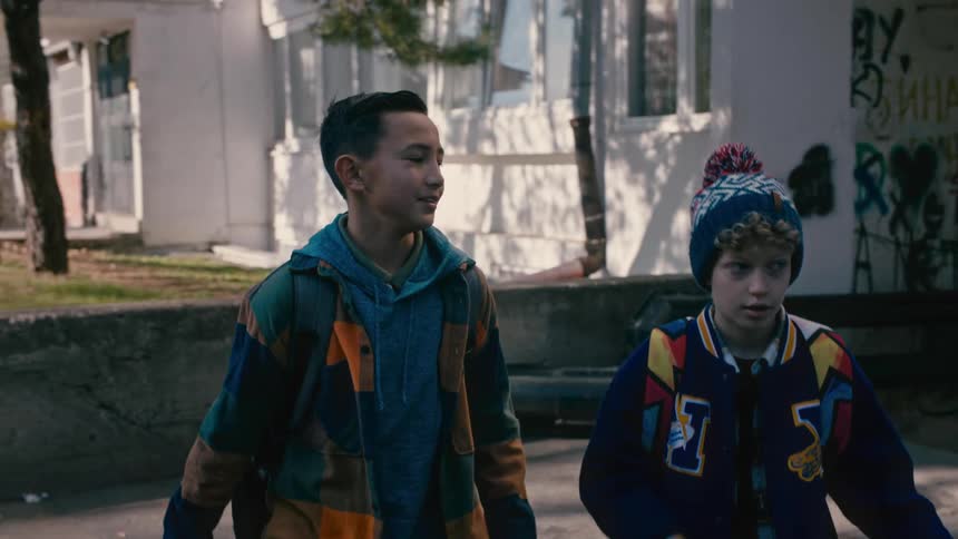 Two little boys are walking down an alley with graffiti and then they start running happily