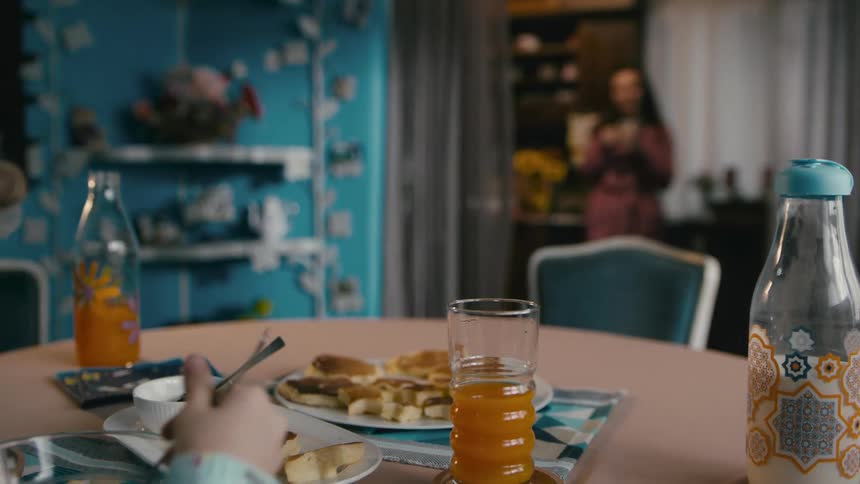 Mother watches his son eating breakfast from the kitchen at morning