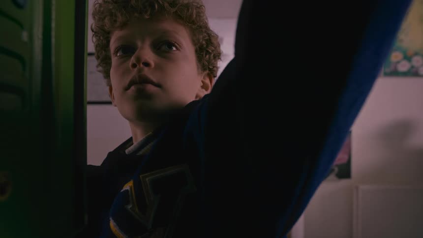 A boy is taking things out of a school locker and some people are behind him