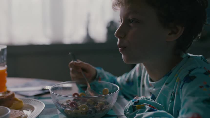 A boy in pajamas is eating cereal from a transparent bowl on a table