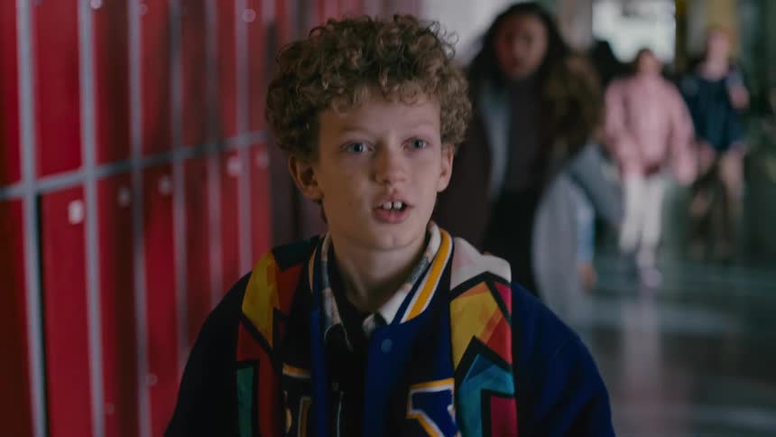 Young boy entering and walking on the school hallway with other students