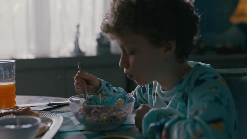 A boy in pajamas is sitting and eating cereal from a transparent bowl
