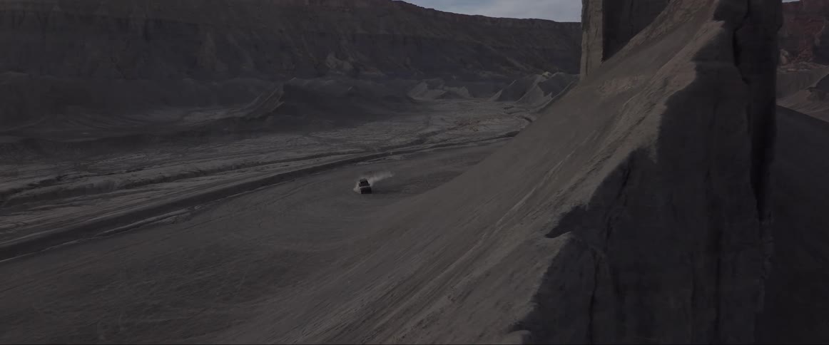 An off road vehicle climbs the slope of a rock formation in the desert