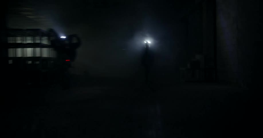 Two people driving motorcycle in an almost completely dark warehouse