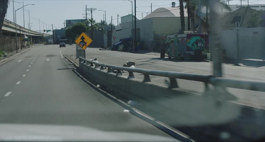 A car drives down a city road near a homeless encampment