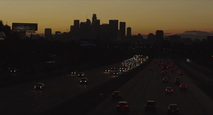 Early evening with the orange sky overlooking traffic on a highway with the silhouette of downtown Los Angeles buildings