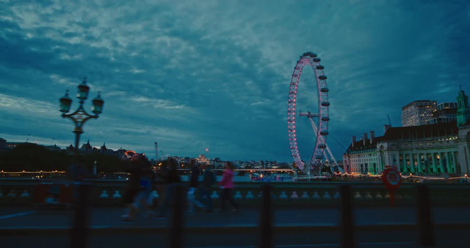 People walk over the bridge by the large ferris wheel
