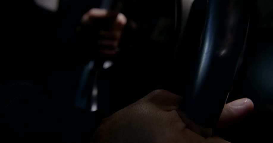 Steering wheel reflects electric lights as person steers vehicle