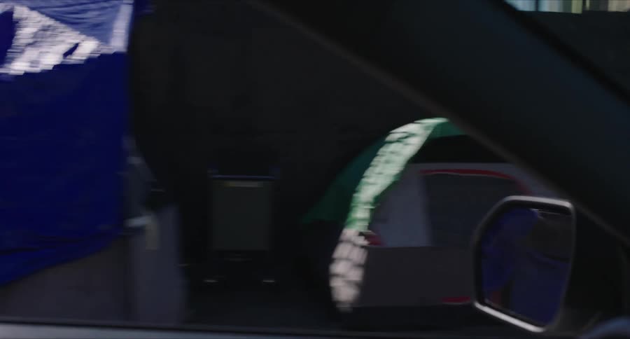 Vehicle drives along street passing multiple tents setup on sidewalk leading to downtown intersection