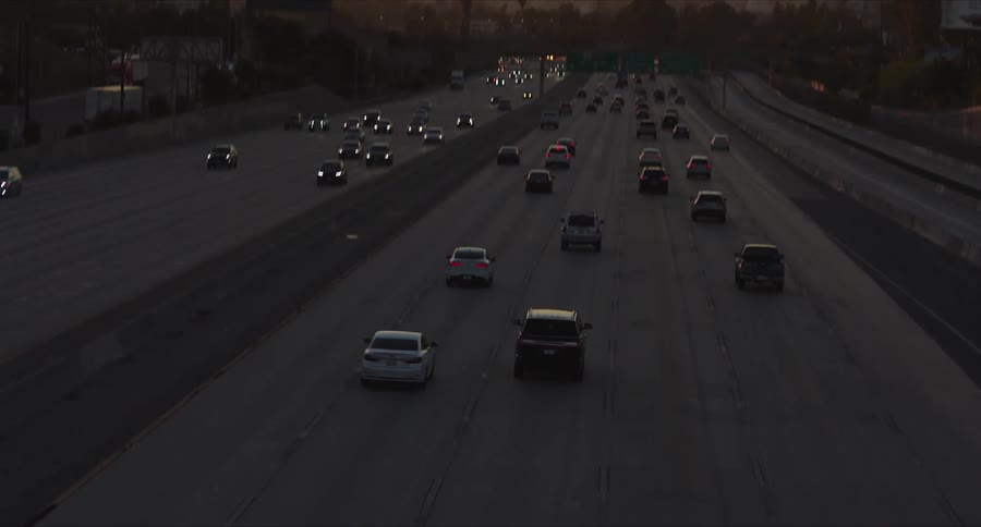 Traffic flows toward and from a hazy Los Angeles skyline under a red tinted sky