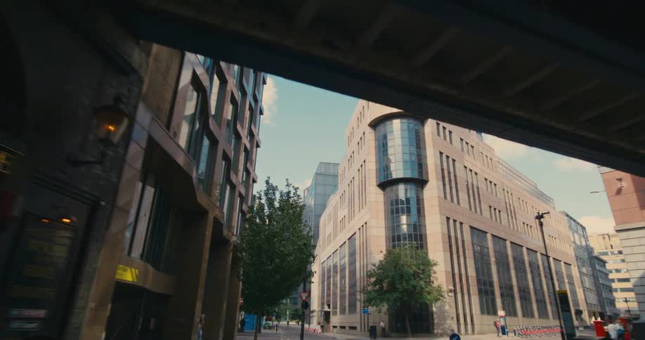 A large corner building with many rounded glass windows and close to an overpass