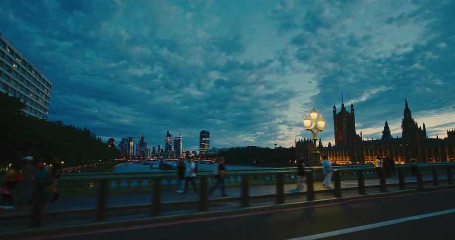 Pedestrians walk across westminster bridge at twilight under a cloudy sky