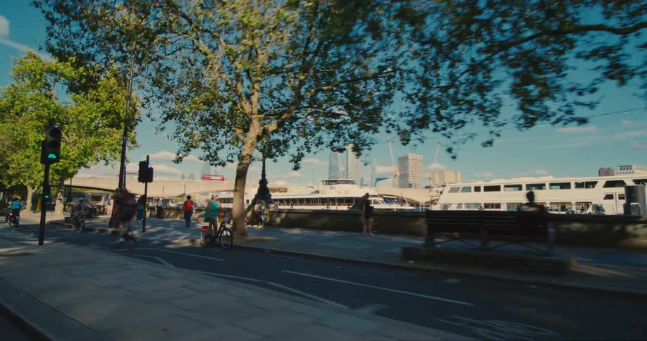 People walking and cycling along the side of streets in cities next to boats on the seafront