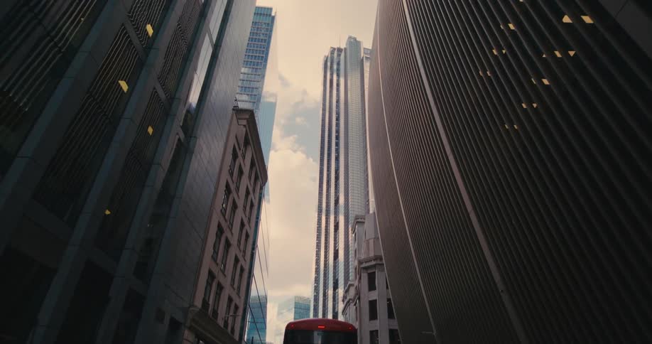 A street in a city center with huge buildings and a red bus passing by