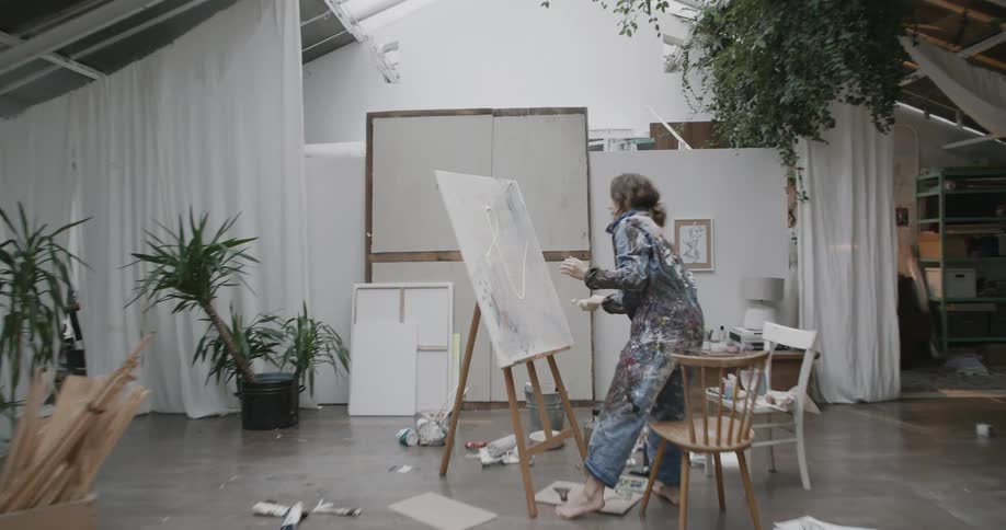 Woman painter throwing white paint on a canvas indoors