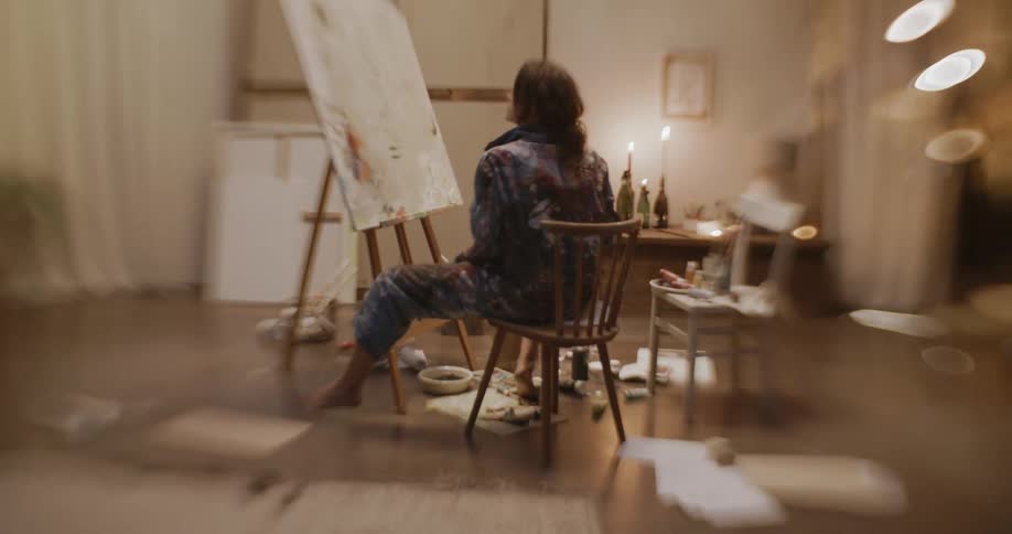 A woman sitting in a chair paints on a large white canvas