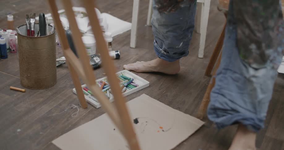 A painter with stained jeans stands in front of an easel